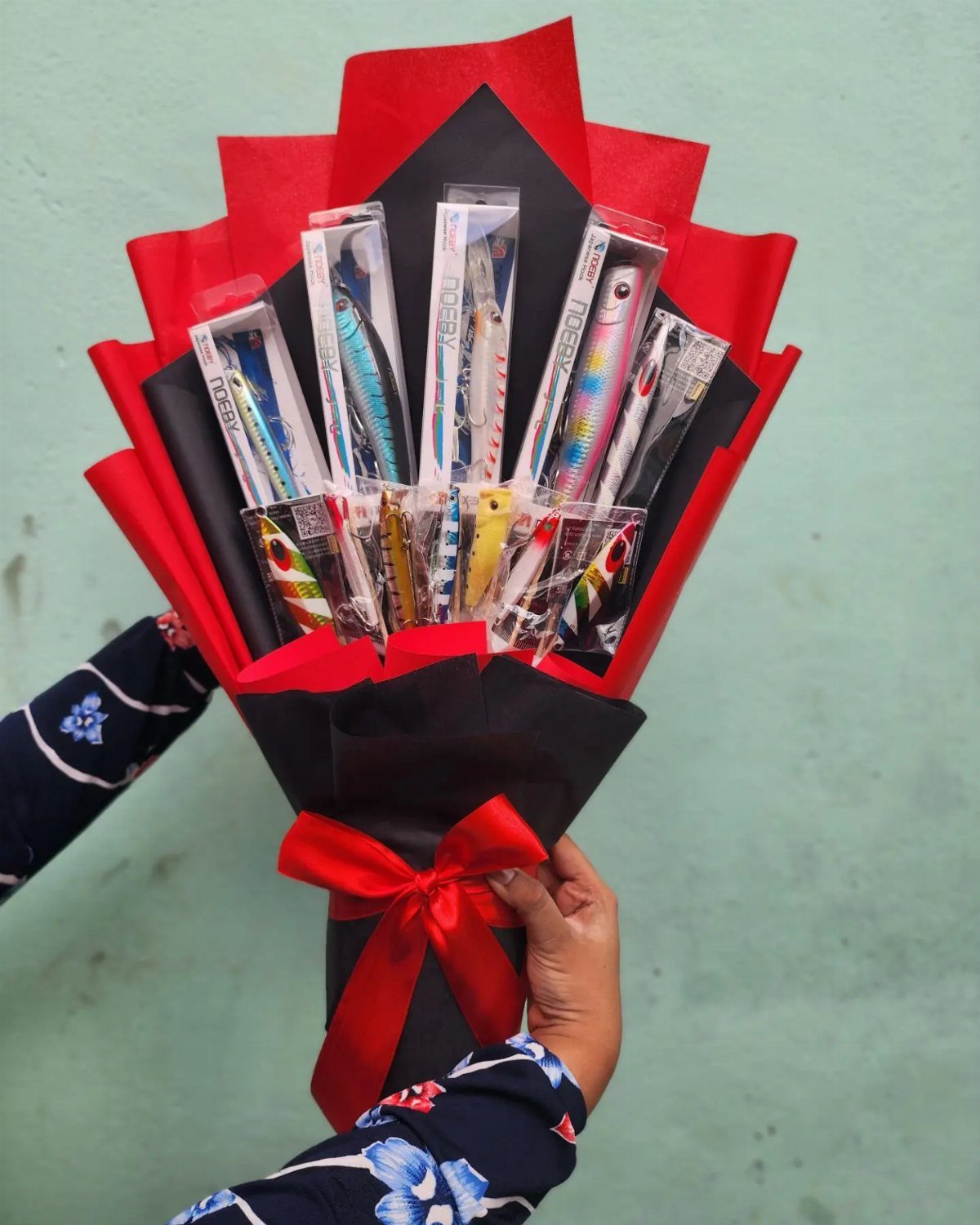 Fishing lures arranged as a bouquet wrapped in black and red paper.
