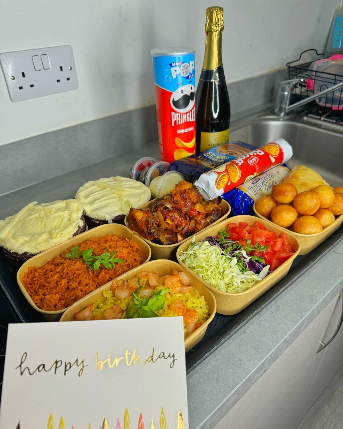 Assorted birthday meal with rice, shrimp, wings, and champagne on a kitchen counter.