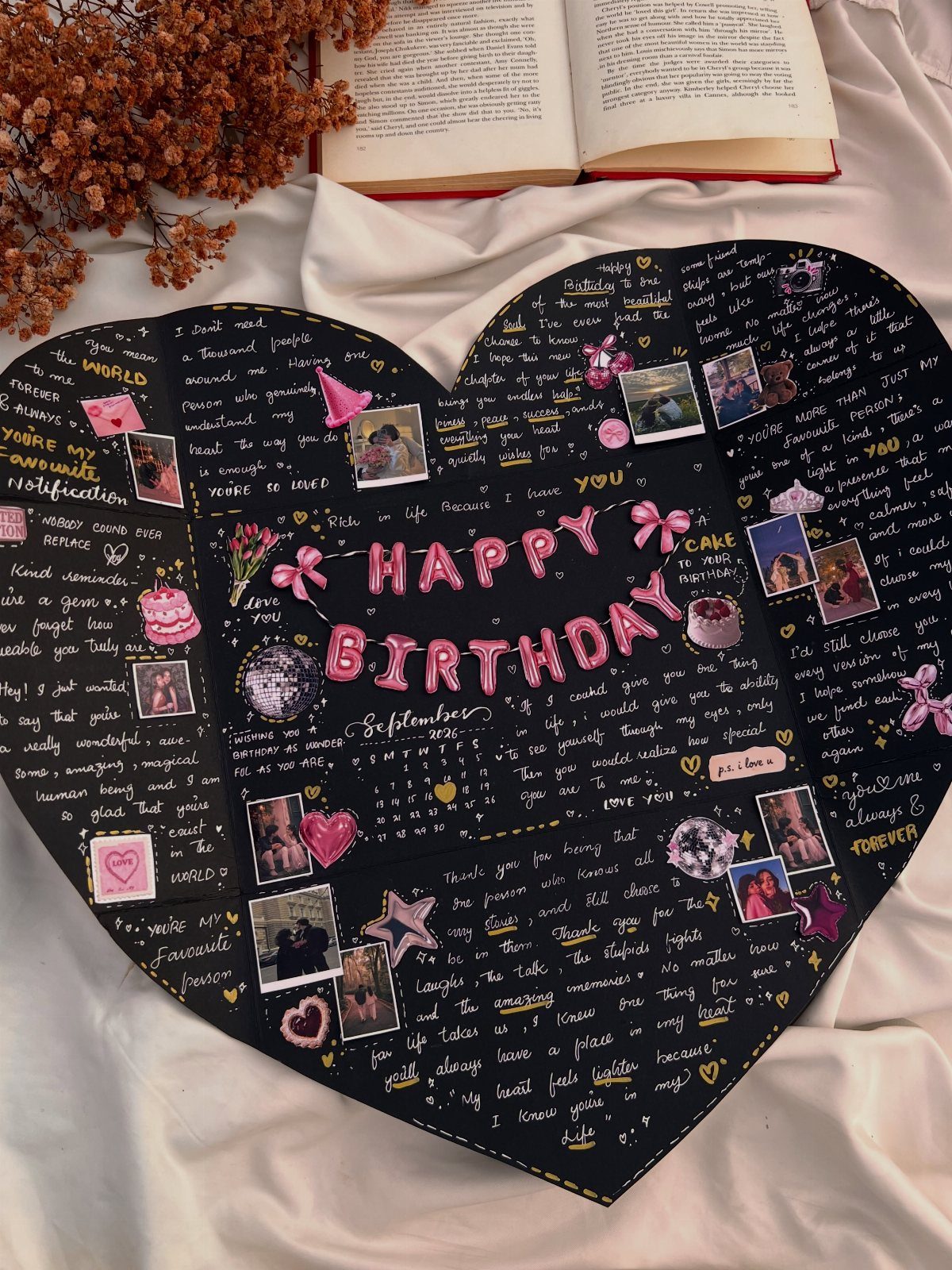 Heart-shaped black scrapbook page with birthday messages, photos, and pink decorations on white fabric.