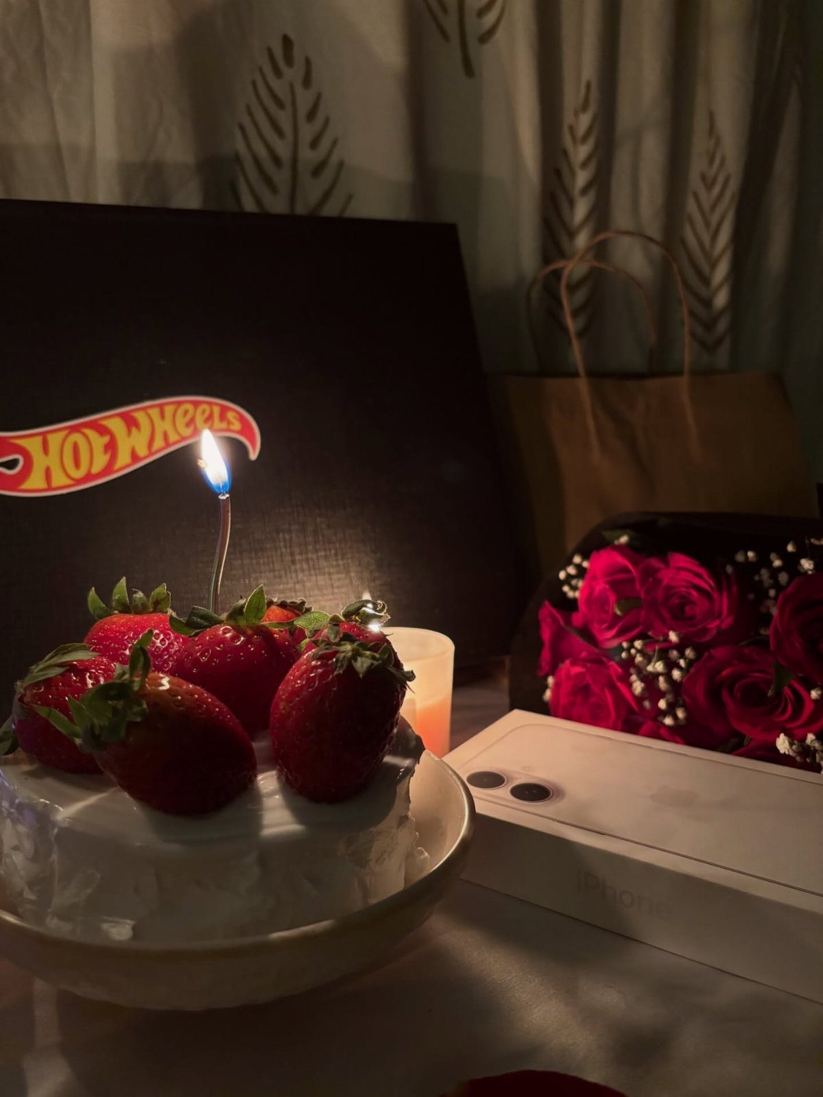 Small strawberry cake with a lit candle, red roses, and Hot Wheels branding.