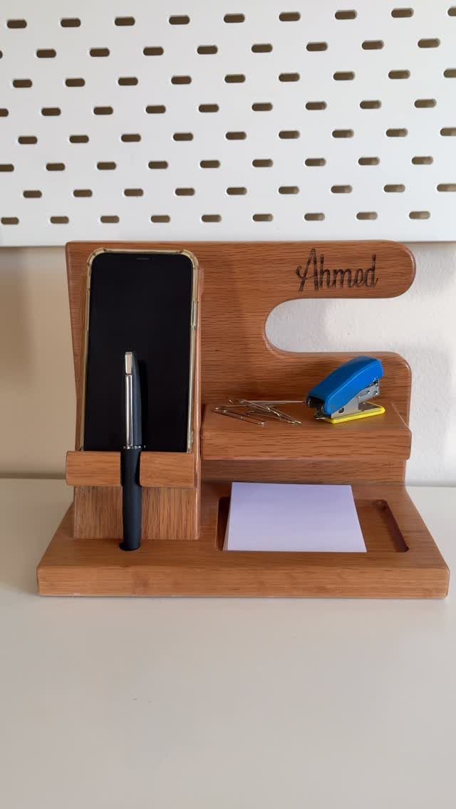 Wooden desk organizer holding a smartphone, pen, sticky notes, and a blue stapler.