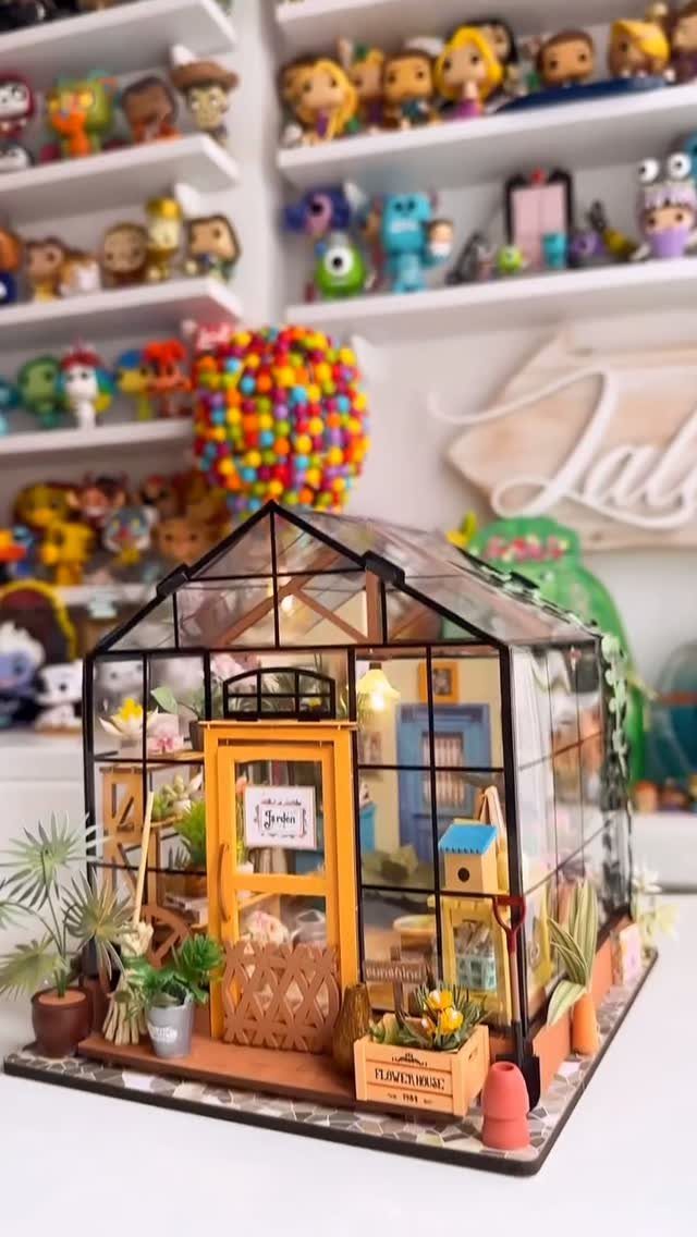 Miniature greenhouse kit with tiny plants and furniture inside a glass enclosure.