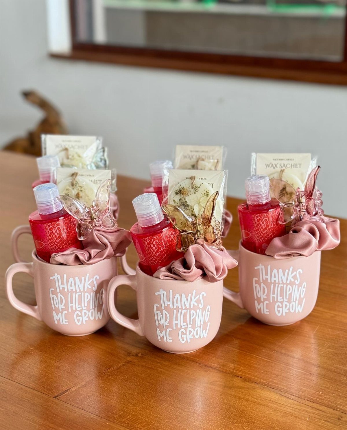 Three pink mugs with personalized text filled with hand sanitizer and wax sachets.
