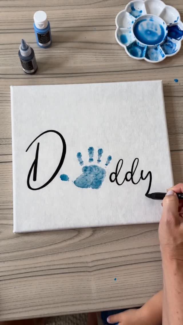 Hand painting Daddy on a white canvas with a blue child's handprint.
