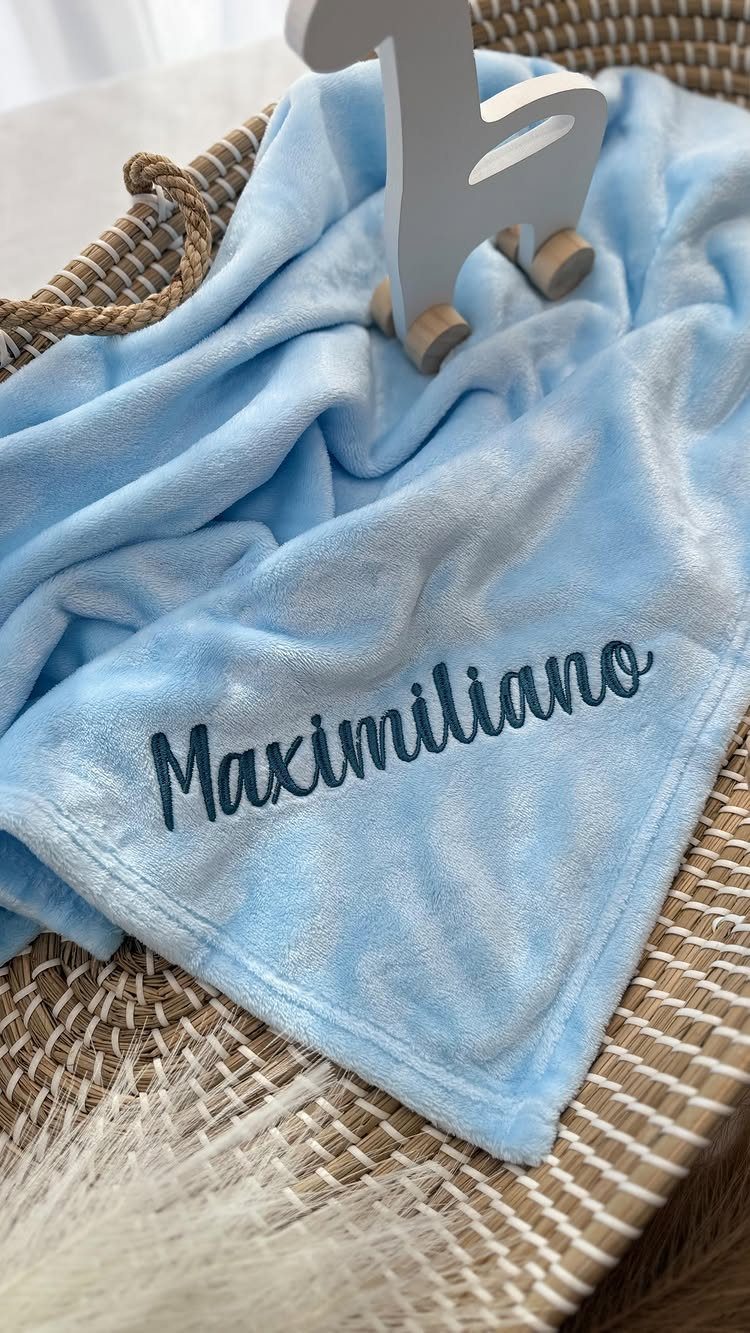Light blue plush blanket with Maximiliano embroidered in dark blue inside a basket.