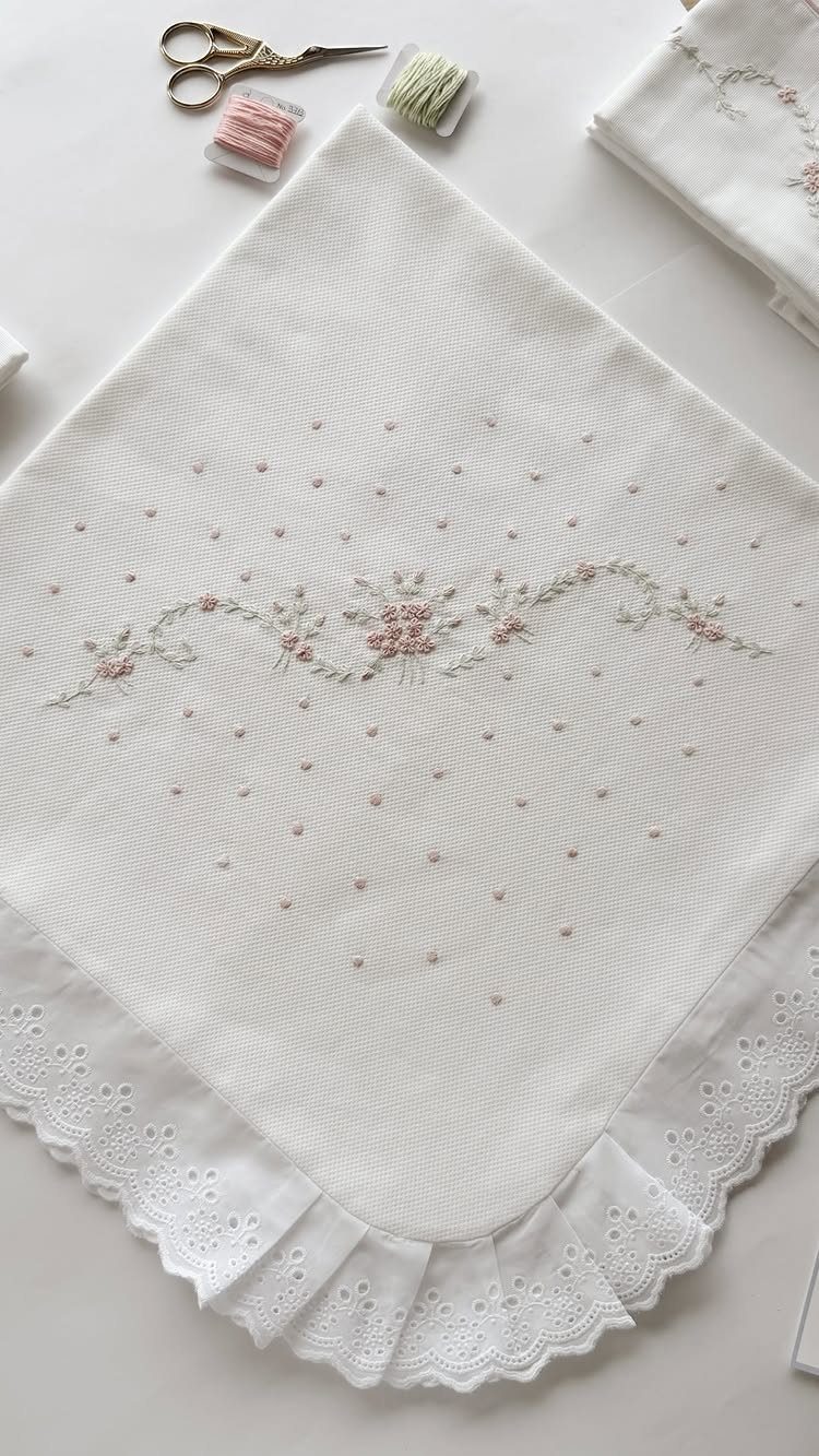 Embroidered white handkerchief with floral patterns and lace trim next to sewing tools