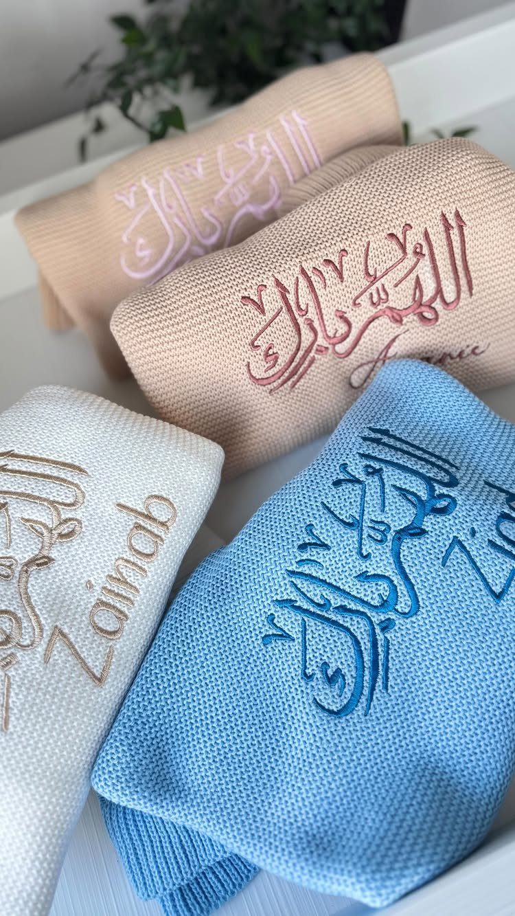 Embroidered knit scarves in blue, white, and beige with Arabic calligraphy and names.