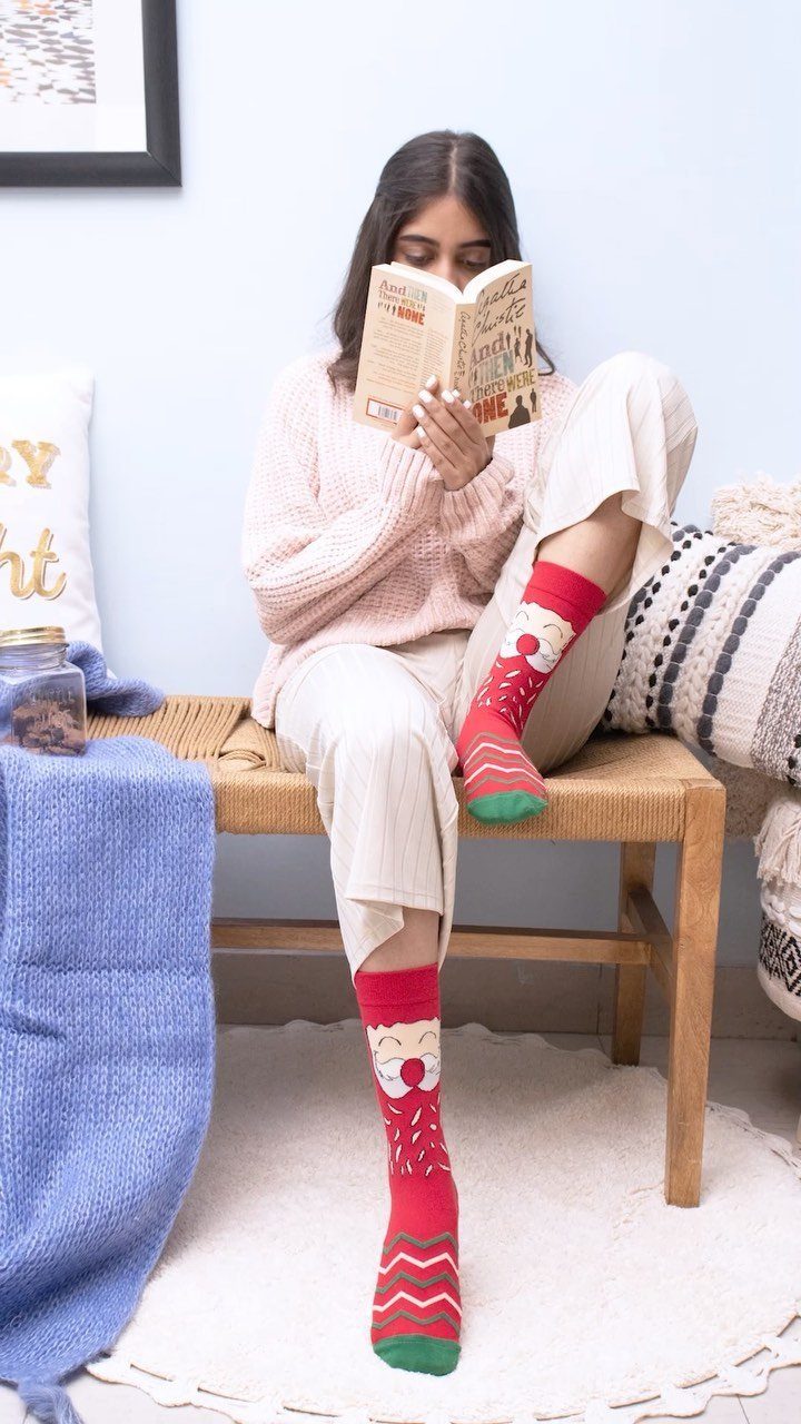 Woman reading a book while wearing red Christmas socks with Santa patterns.