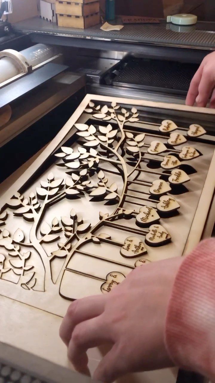 Wooden laser-cut family tree with heart-shaped name plaques being handled by a person