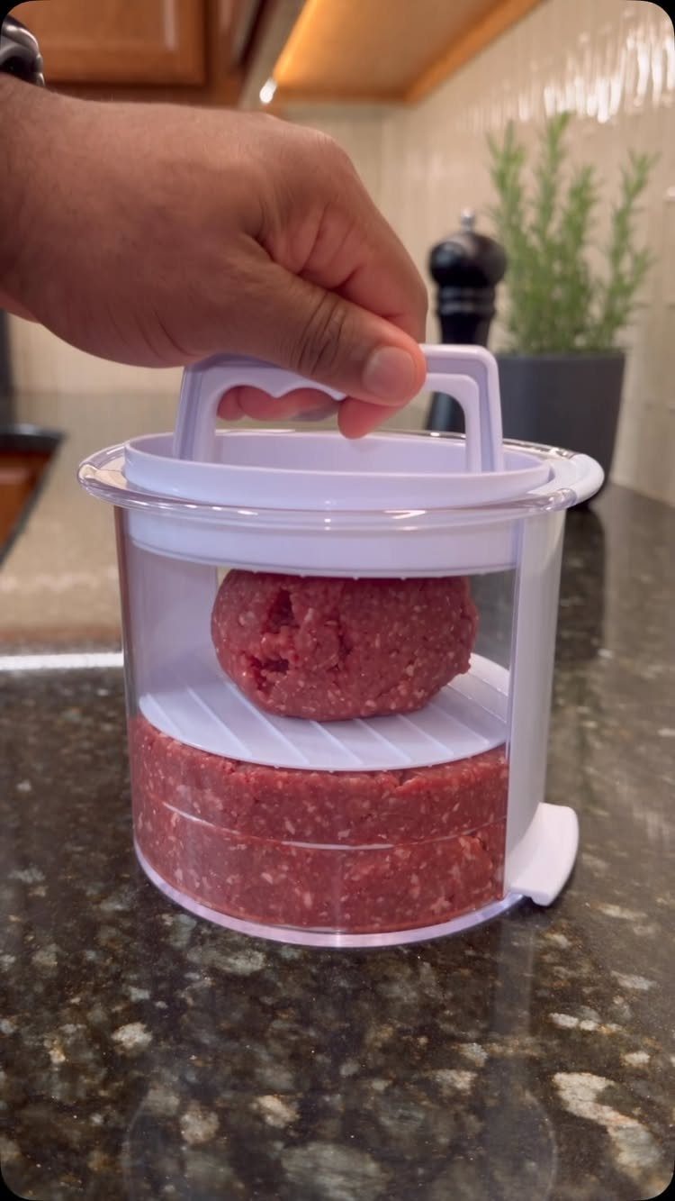 Hand using a white plastic burger patty maker with raw ground beef.