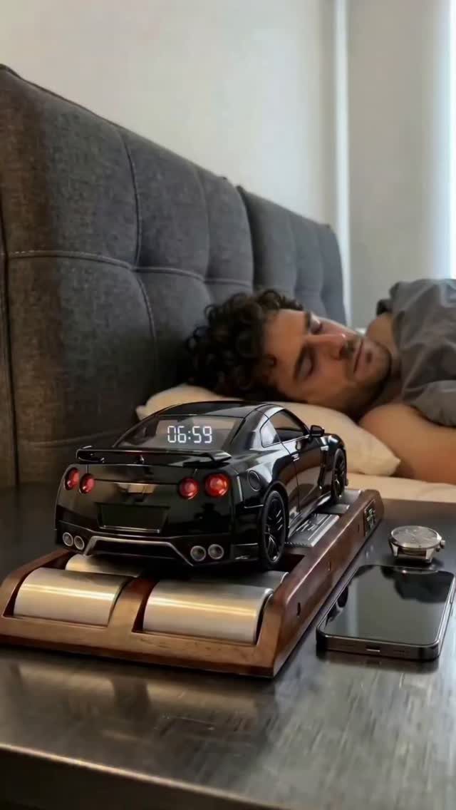 Black sports car digital clock on a wooden base next to a sleeping man