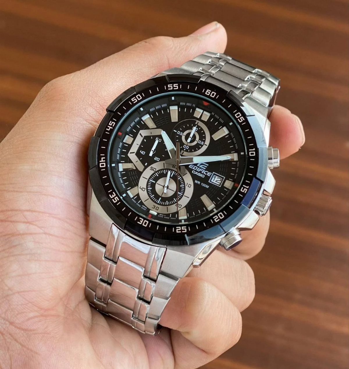 Casio Edifice chronograph watch with silver metal band held in a person's hand.