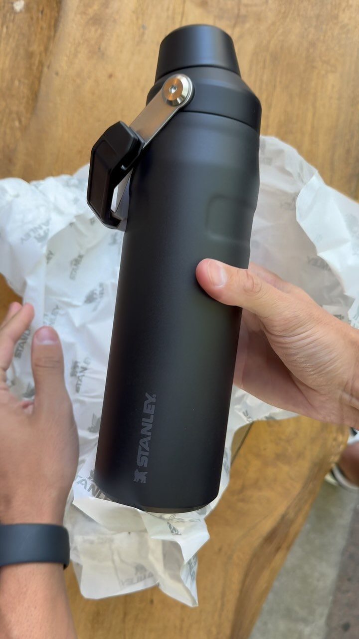 Matte black Stanley vacuum flask held by hands over white tissue paper.