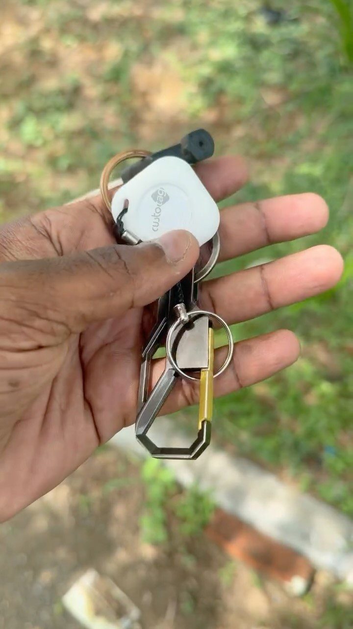 Hand holding a set of keys with a white electronic tracking device.