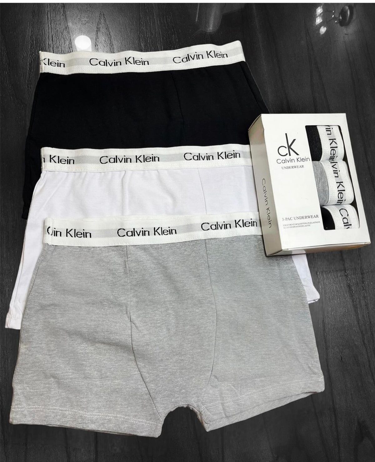 Men's boxer briefs in black, white, and grey with a branded product box.