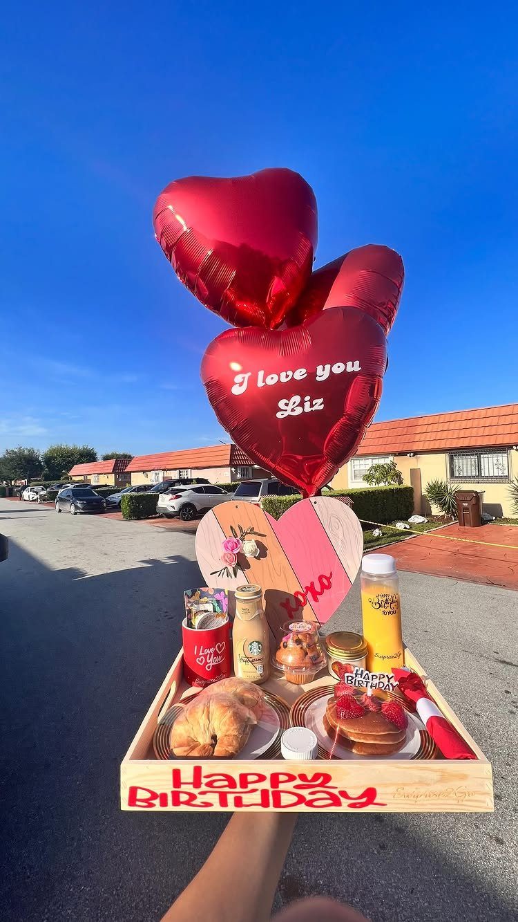Birthday breakfast tray with pancakes, pastries, and red heart balloons outdoors