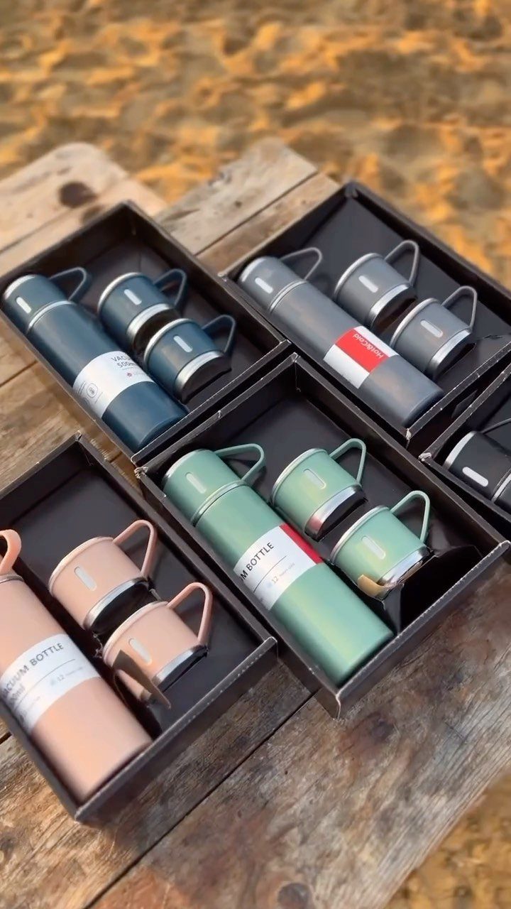 Four colorful vacuum bottle and cup gift sets in black boxes on wood.