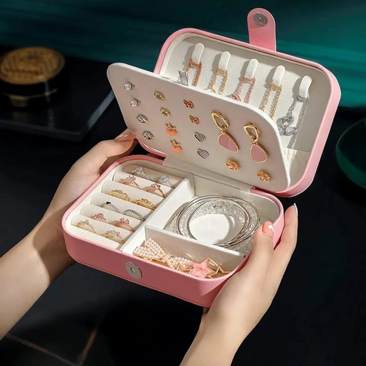 Small pink portable jewelry case held in hands, filled with rings and necklaces.