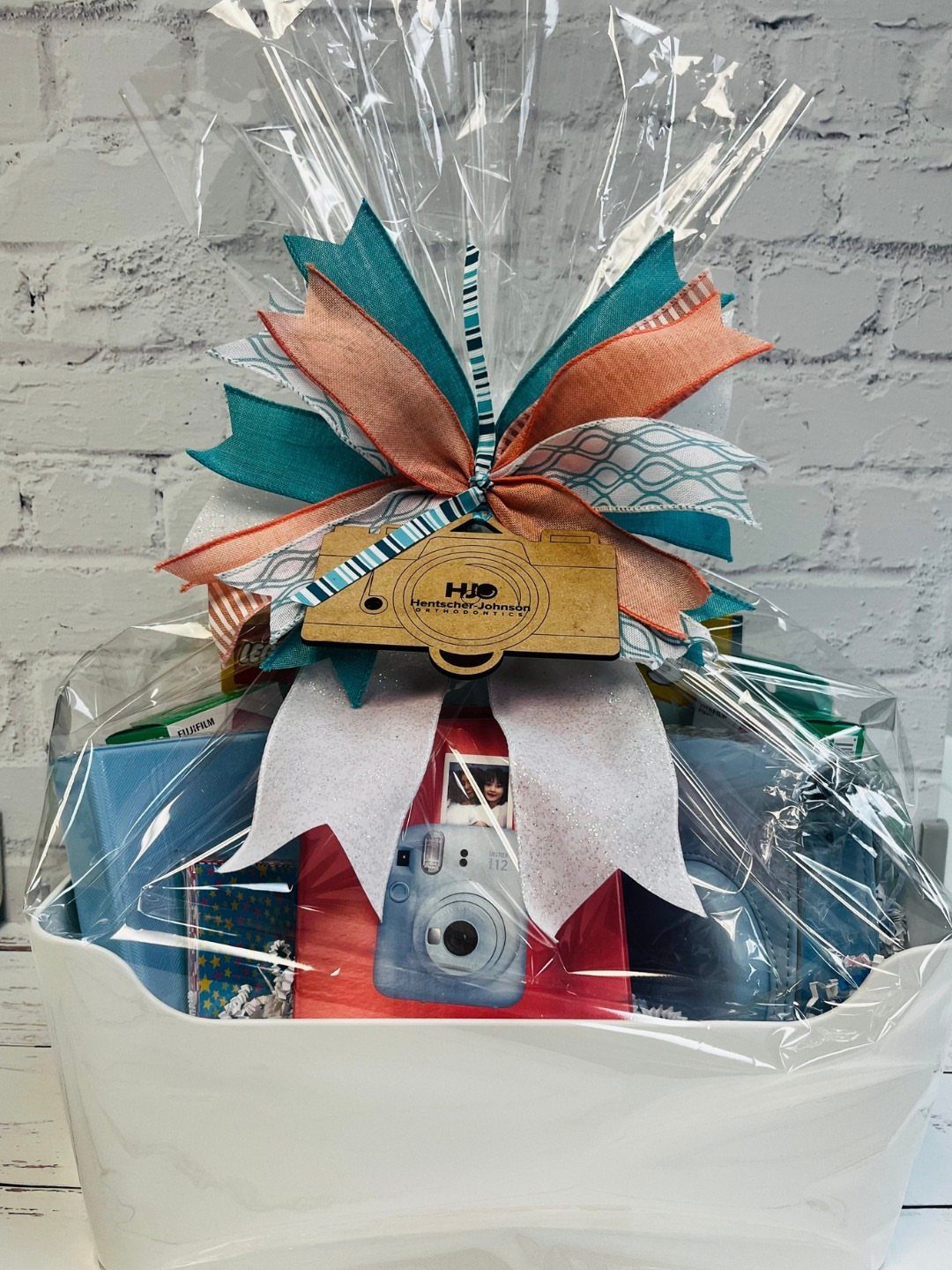 Gift basket wrapped in cellophane with a blue instant camera and colorful bow.