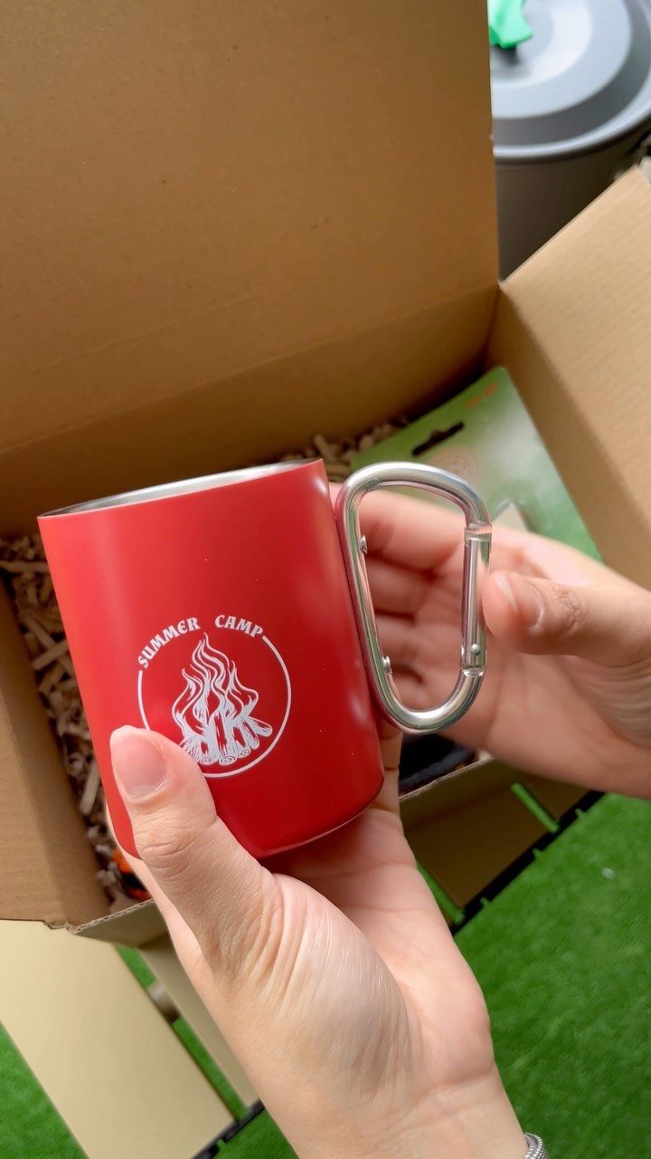 Red metal camping mug with carabiner handle held over a shipping box