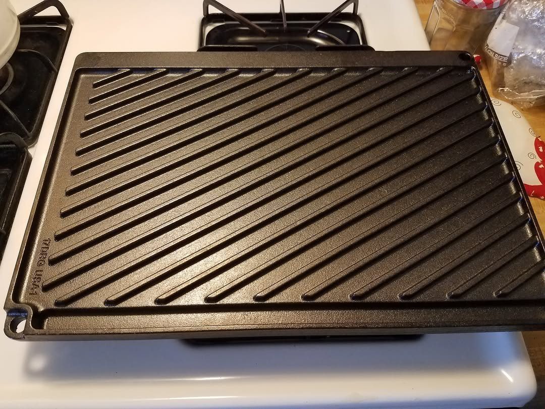Black cast iron square grill pan with ridges on a white stovetop