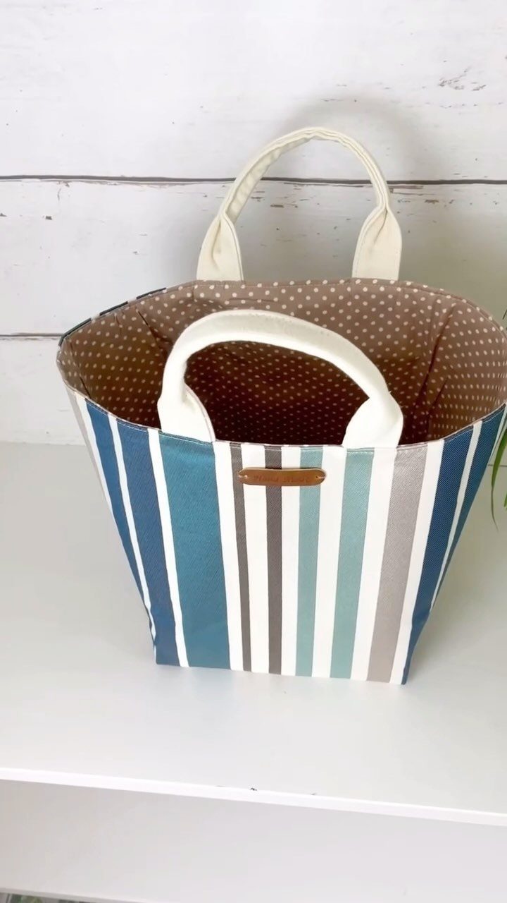 Striped fabric storage basket with polka-dot lining and white handles on white shelf