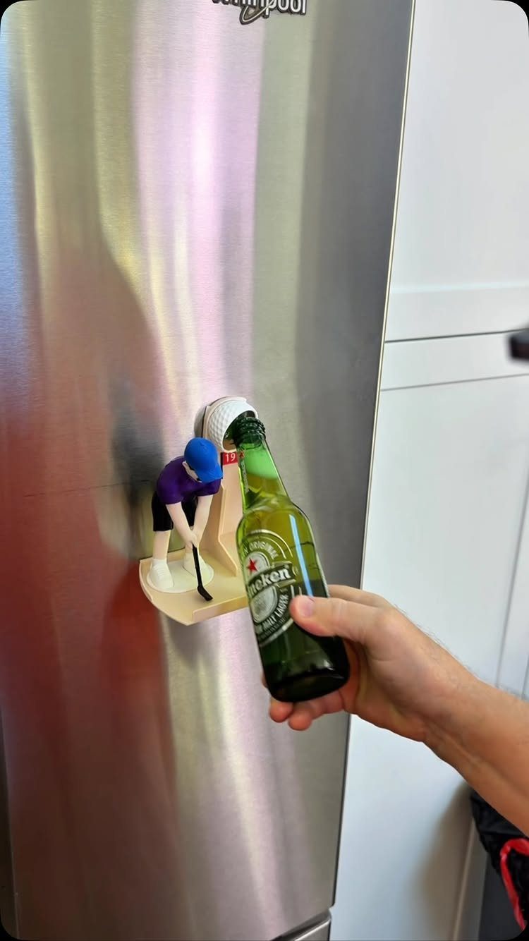 Hand holding a beer bottle next to a hockey player bottle opener on a fridge