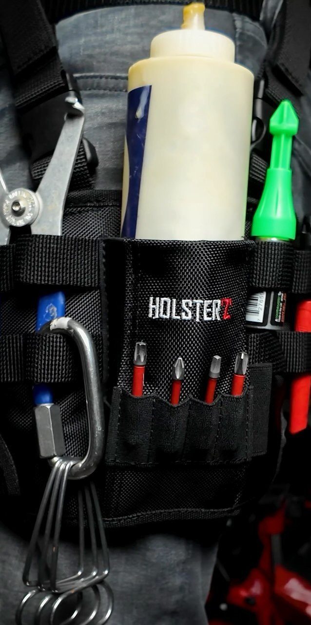 Black tool holster worn on waist containing screwdrivers and a white bottle.