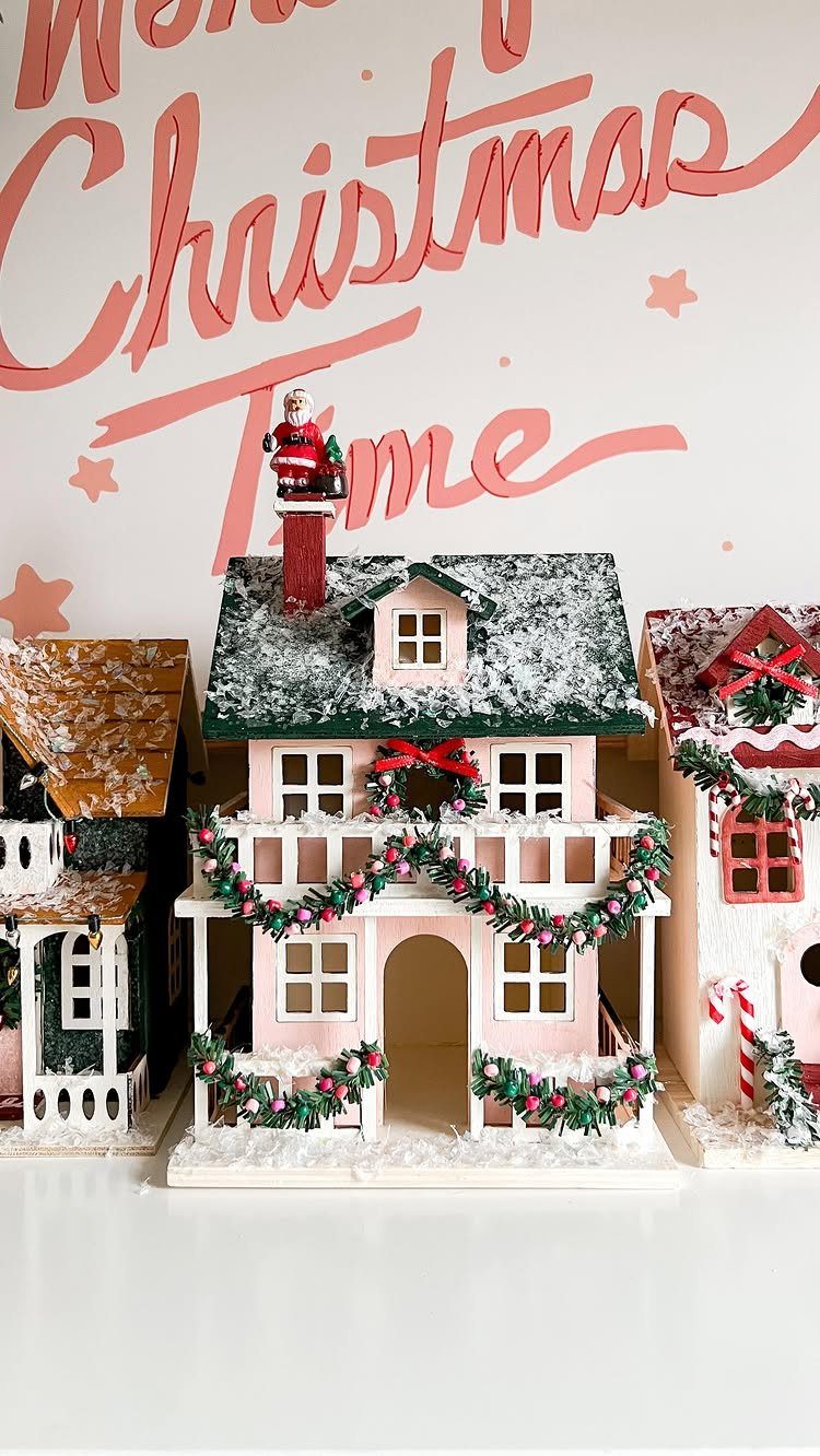Miniature Christmas village houses with snow-covered roofs and festive green garlands.