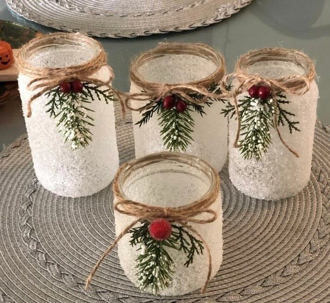 Frosted white glitter glass jars decorated with twine bows and evergreen sprigs.