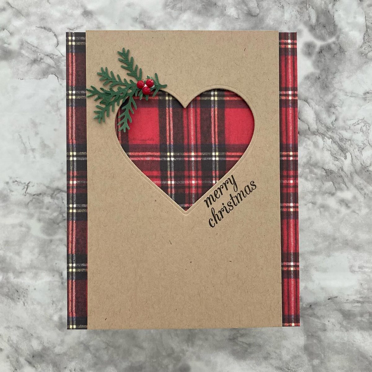 Handmade Christmas card with a heart cutout showing red plaid and berry sprig.
