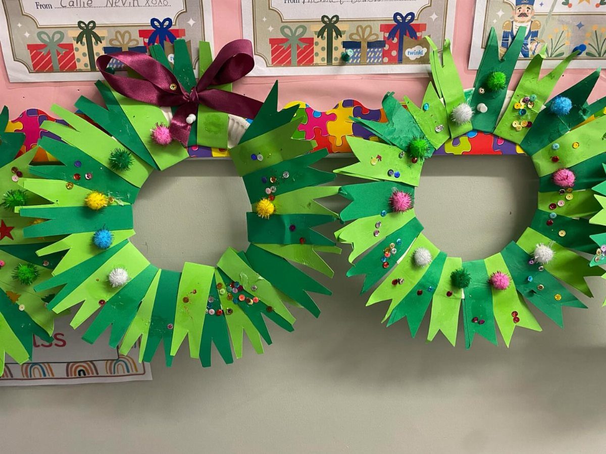 Two green paper plate Christmas wreaths decorated with colorful pom poms and sequins.