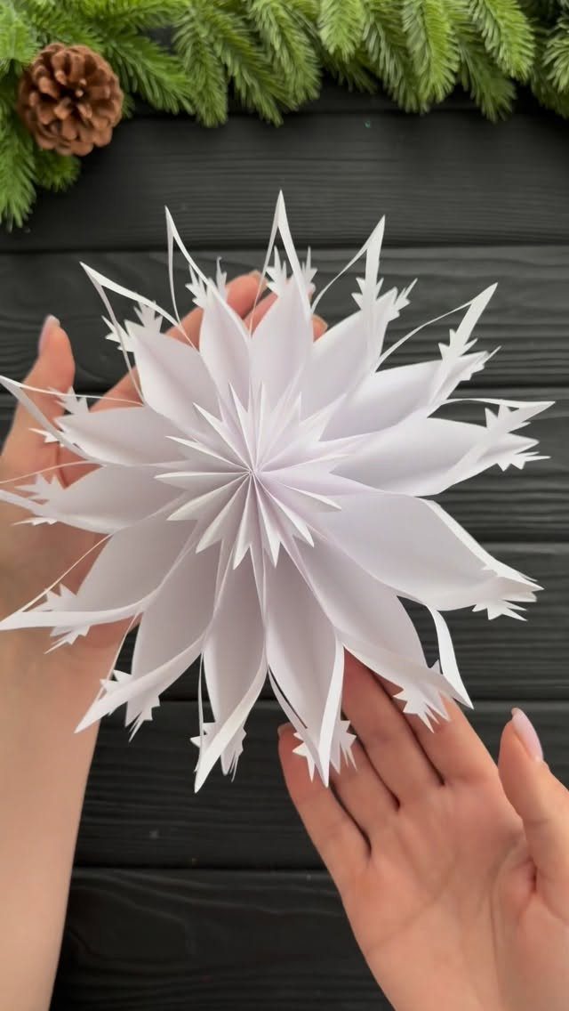 White 3D paper snowflake held by two hands against a dark wooden background
