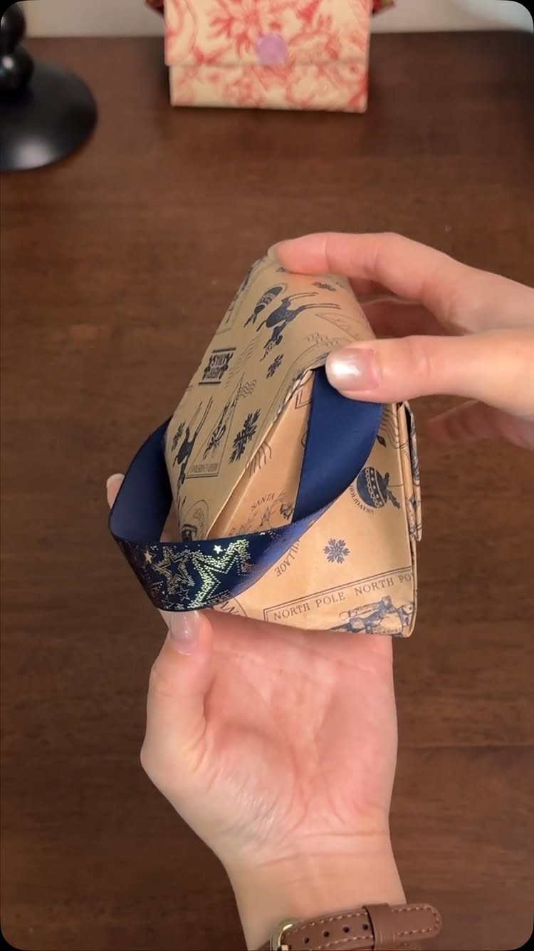 Wrapped gift box with blue illustrations and a dark blue ribbon held by hands.