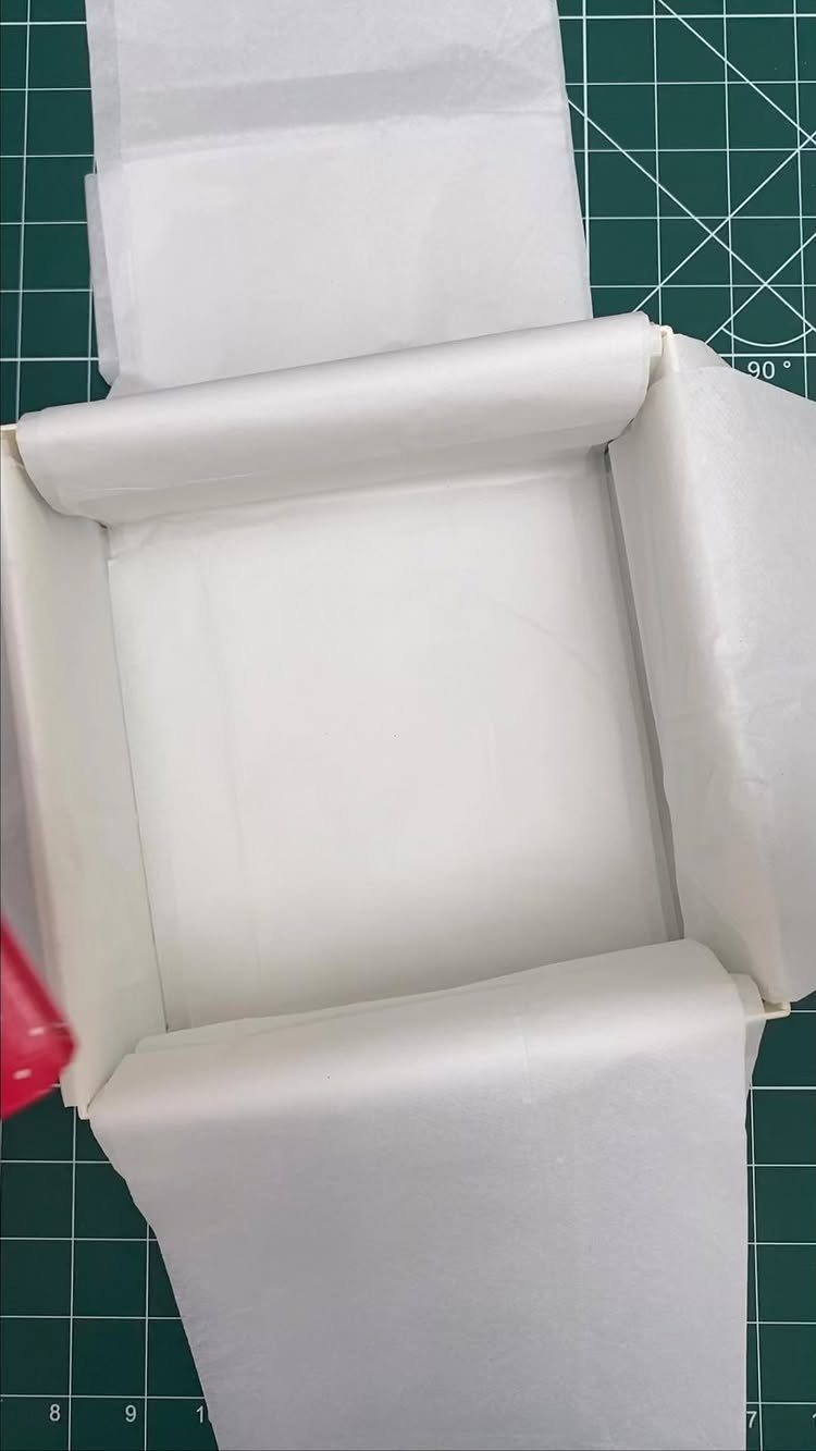 White gift box lined with white tissue paper on a green grid mat