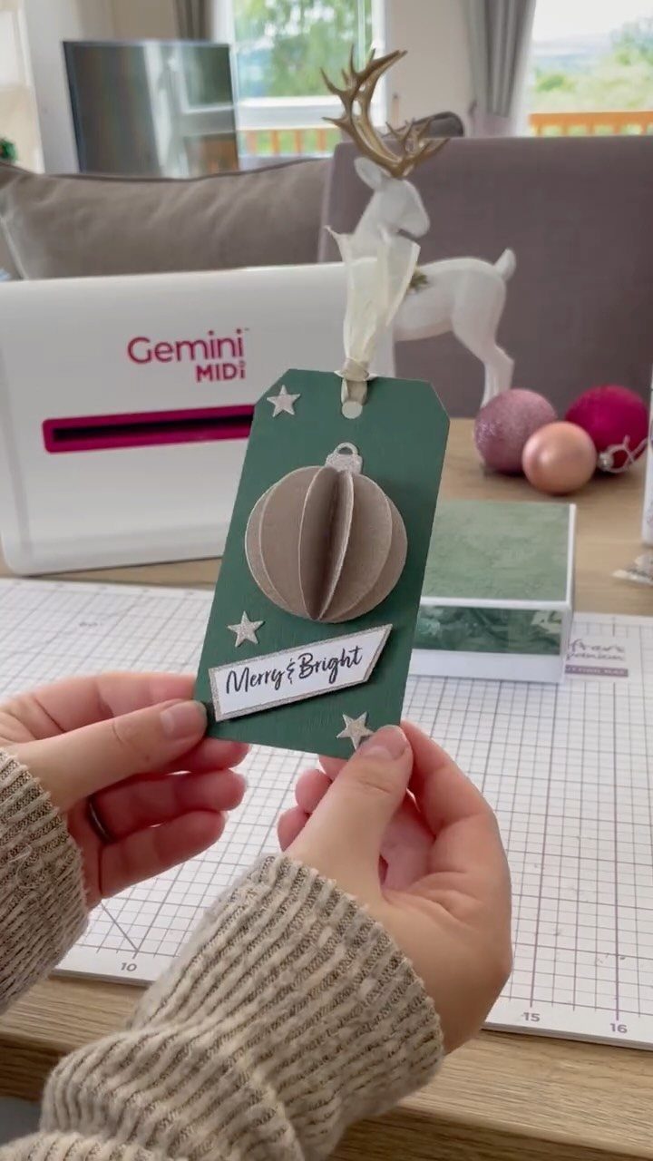 Green gift tag with 3D ornament and stars held by two hands.
