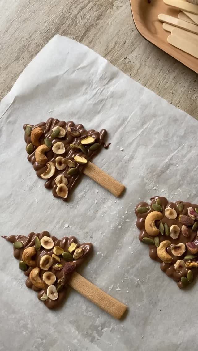 Chocolate Christmas tree treats topped with mixed nuts on white parchment paper