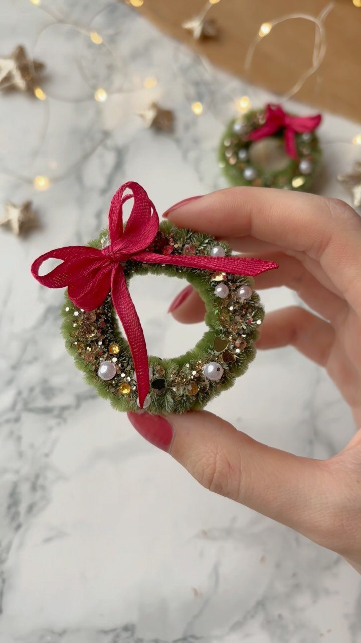 Small handmade green pipe cleaner wreath ornament with red ribbon and pearl beads.