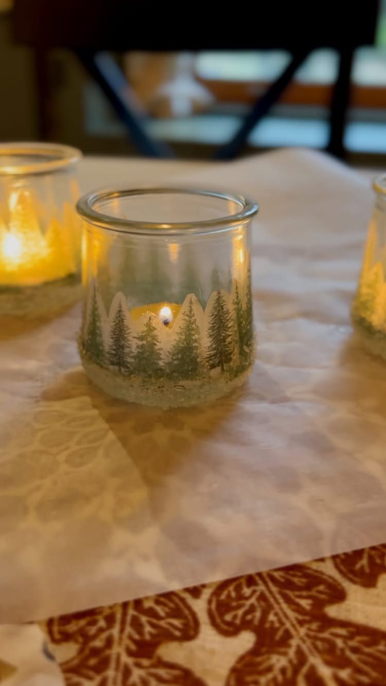 Glass candle holders with painted pine trees and crystalline salt bases on tablecloth