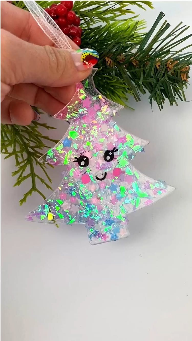 Glittery resin Christmas tree ornament with a cute face held by a hand