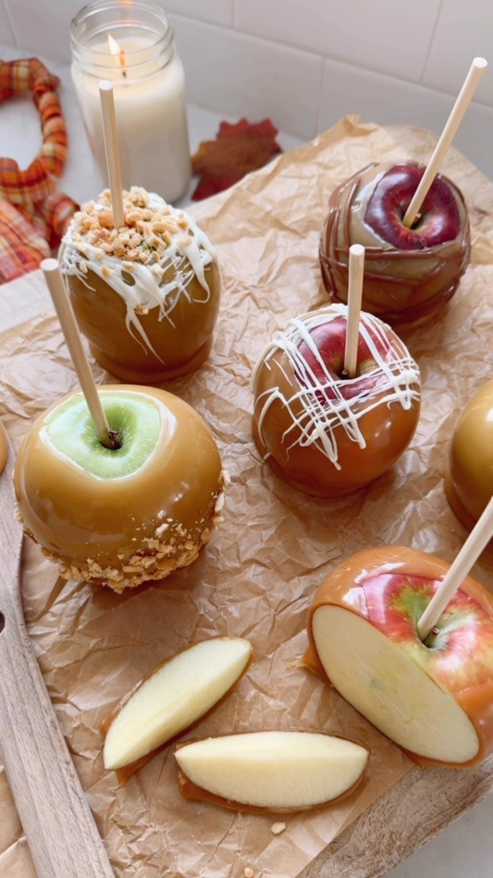 Caramel apples with white chocolate drizzle and nuts on parchment paper.
