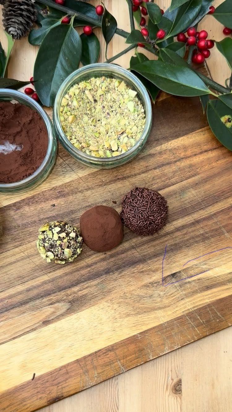Chocolate truffles with pistachio and cocoa coatings on a wooden board with berries.