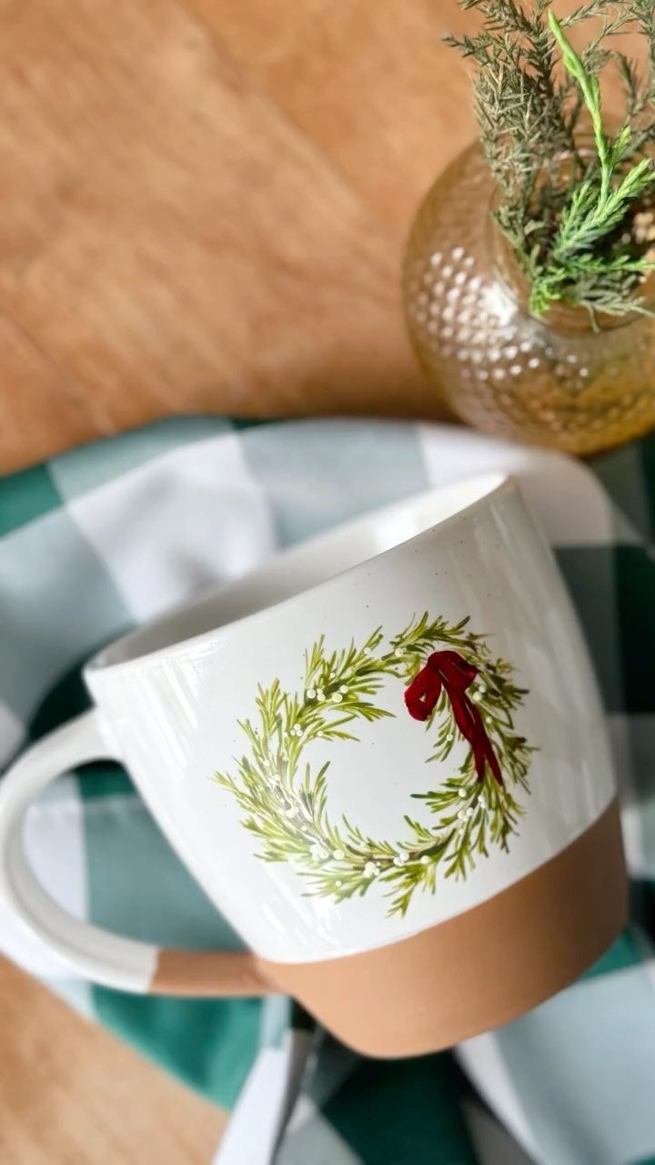 White ceramic mug with a painted Christmas wreath and red bow on checkered cloth