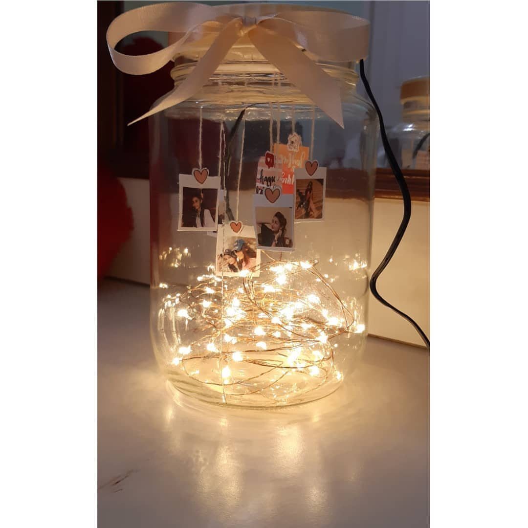 Glass jar with fairy lights and suspended photographs tied with a white ribbon.