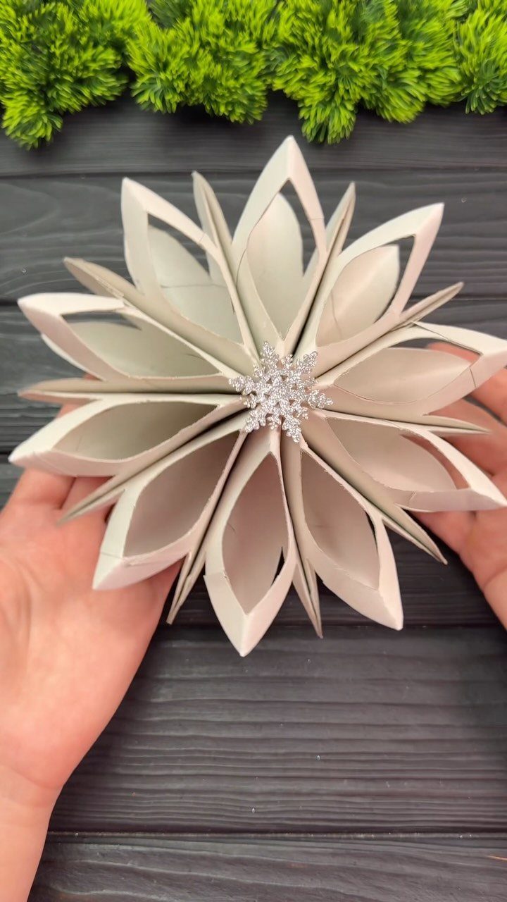 White star-shaped cardboard ornament with a sparkling snowflake center held by two hands.