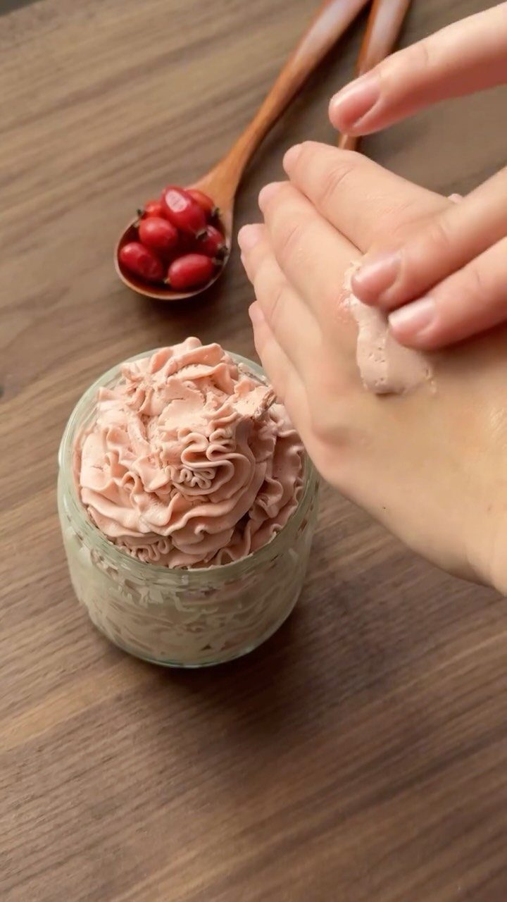 Whipped pink body butter in a glass jar being applied to a hand.