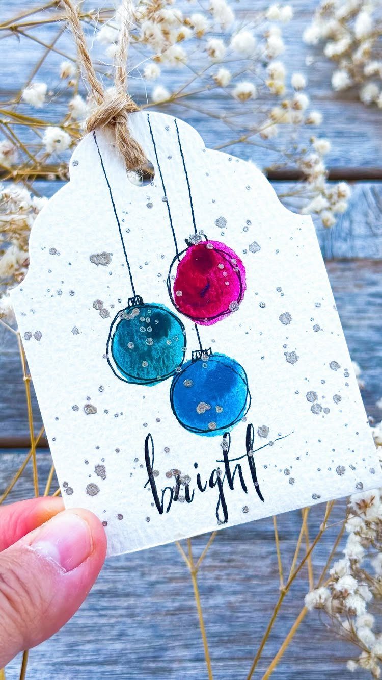 Handmade white gift tag with painted colorful ornaments and the word bright.