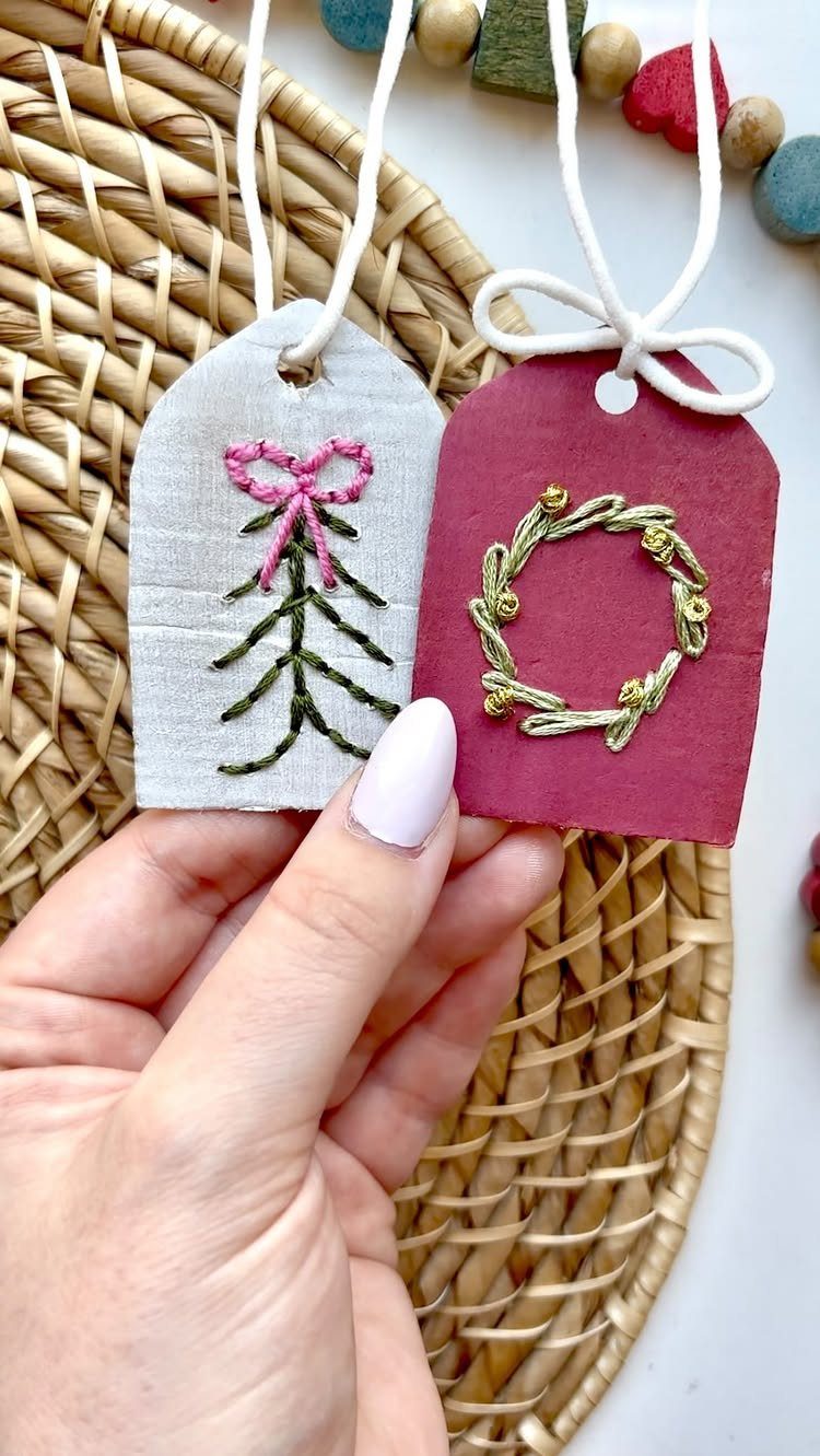 Two fabric gift tags with embroidered Christmas designs held by a hand.