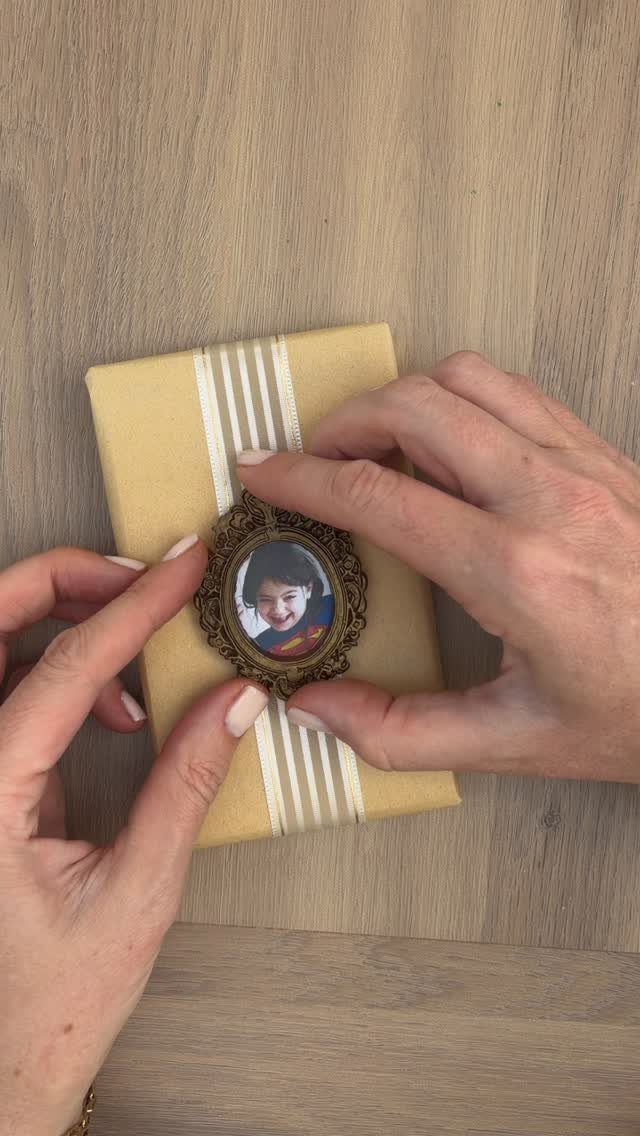 Hands attaching a small framed photo tag to a brown wrapped gift package.