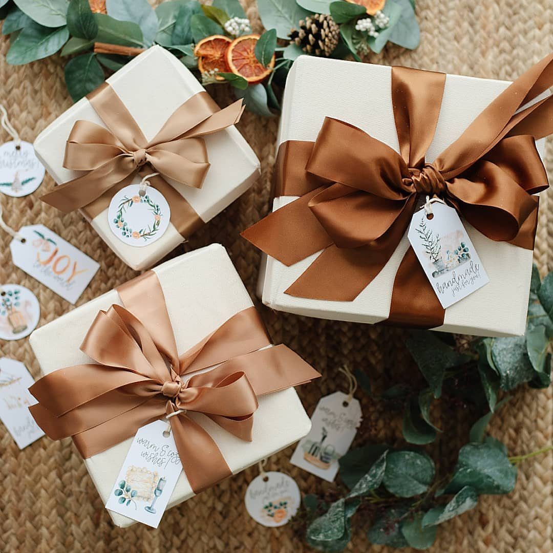 White gift boxes with bronze ribbons and printed floral gift tags on knitted fabric